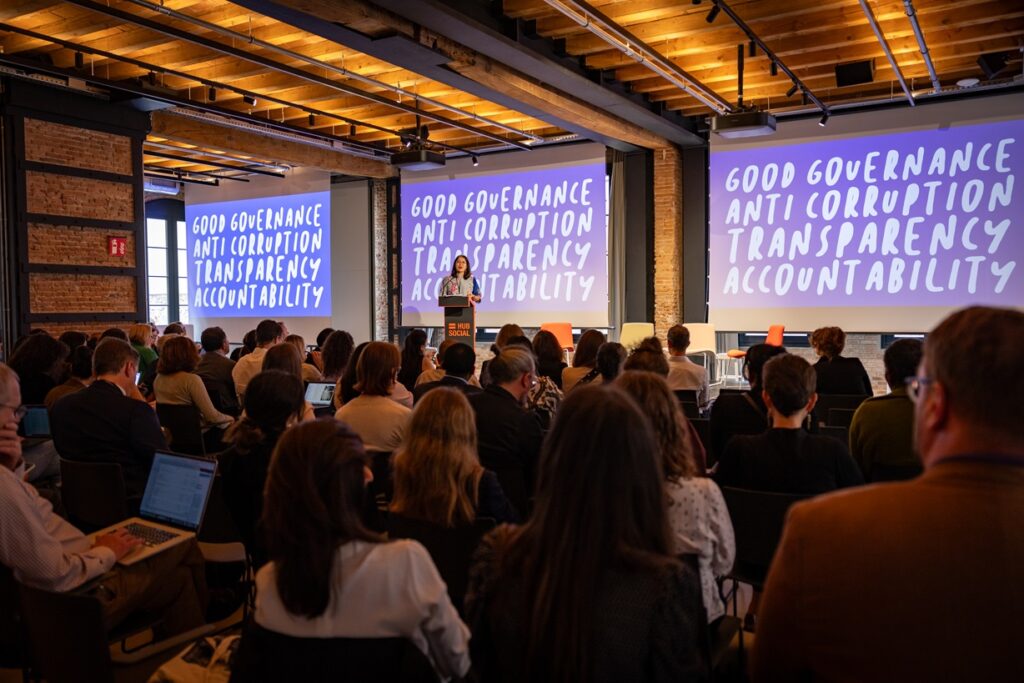Tricia Yeoh delivering her keynote address at the OTT Conference 2024. She stands at the podium, on the screens behind her the slides read "Good governance, transparency, anti-corruption and accountability". 